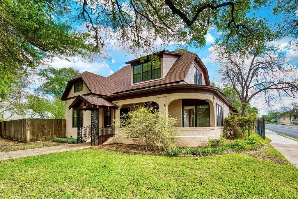 A two-story beige house with a brown roof, a curved porch, and green grass.