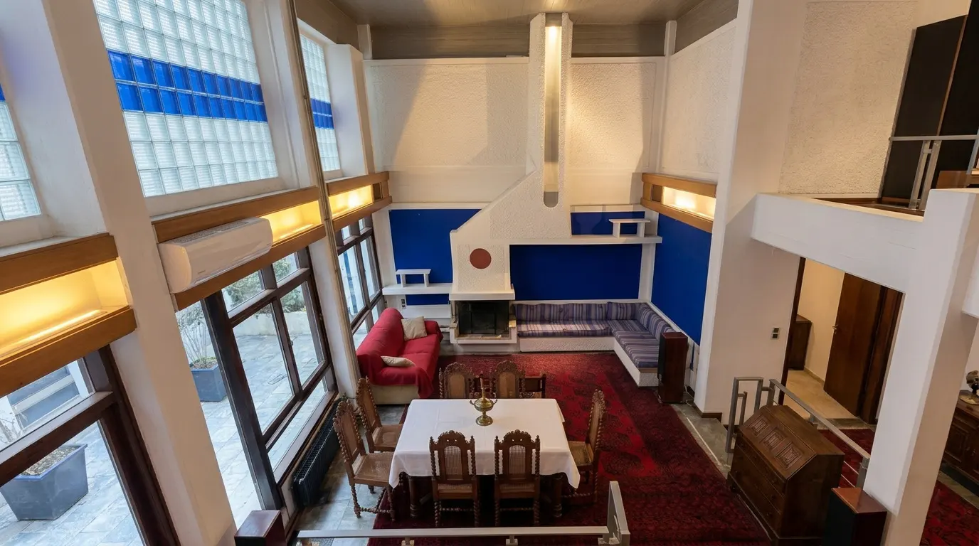 A high-angle view of a modern living room with a dining table, red rug, blue accent wall, and large windows.