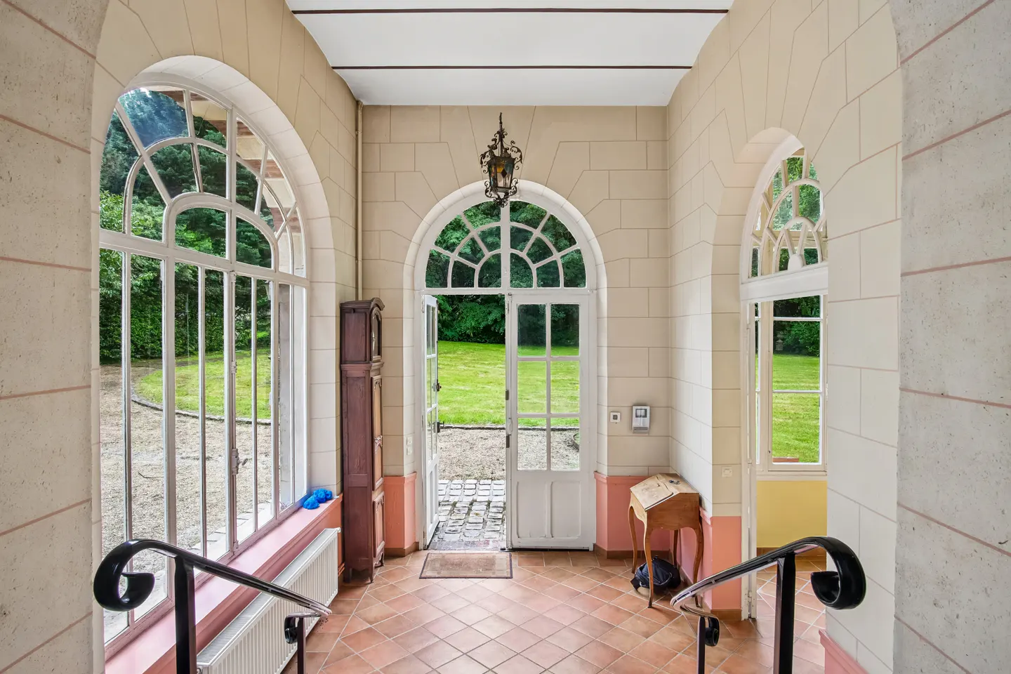 Bright entryway with tiled floor, arched windows, and open glass doors leading to a lush green garden.