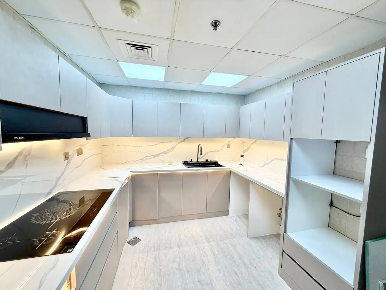 Modern kitchen with white cabinets, marble-patterned countertops, a black stovetop, and a drop ceiling with recessed lights.