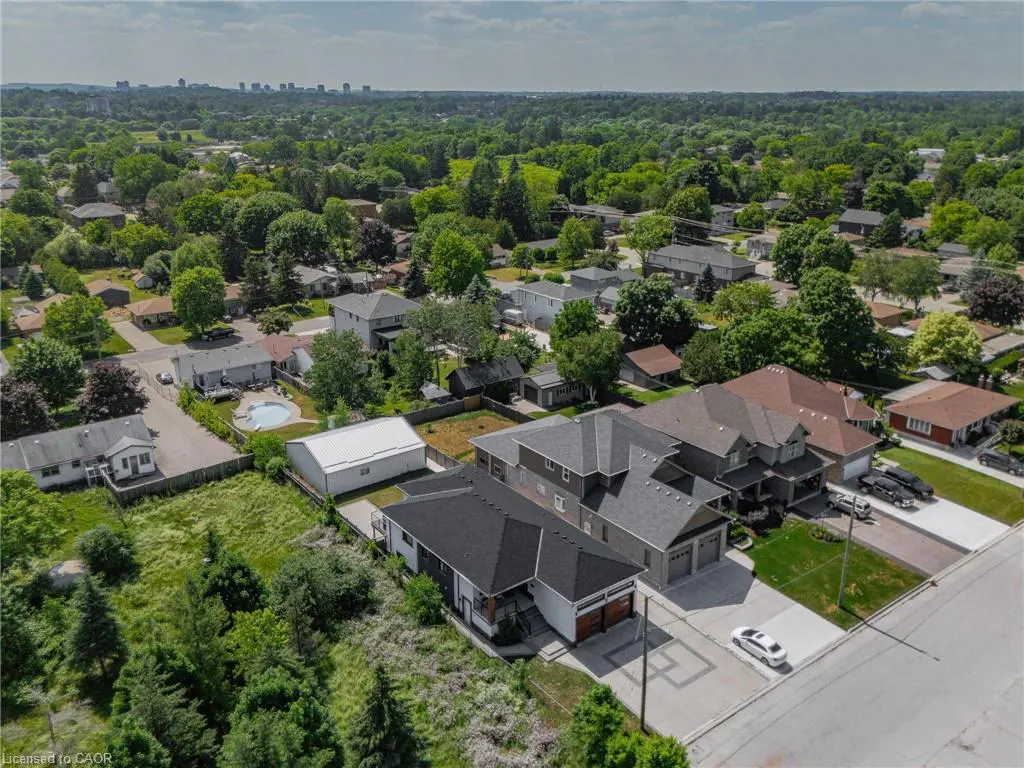 Aerial view of a suburban neighborhood with houses, green trees, and a distant city skyline.