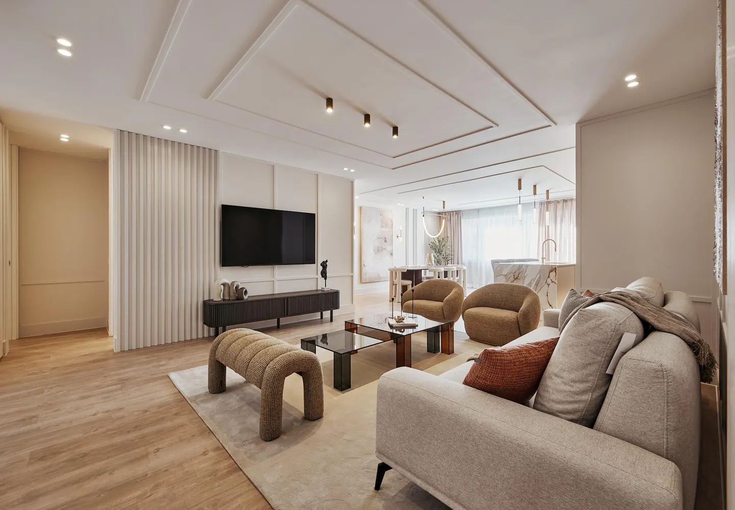 A modern living room with a beige sofa, brown chairs, a black TV, and a glass coffee table.