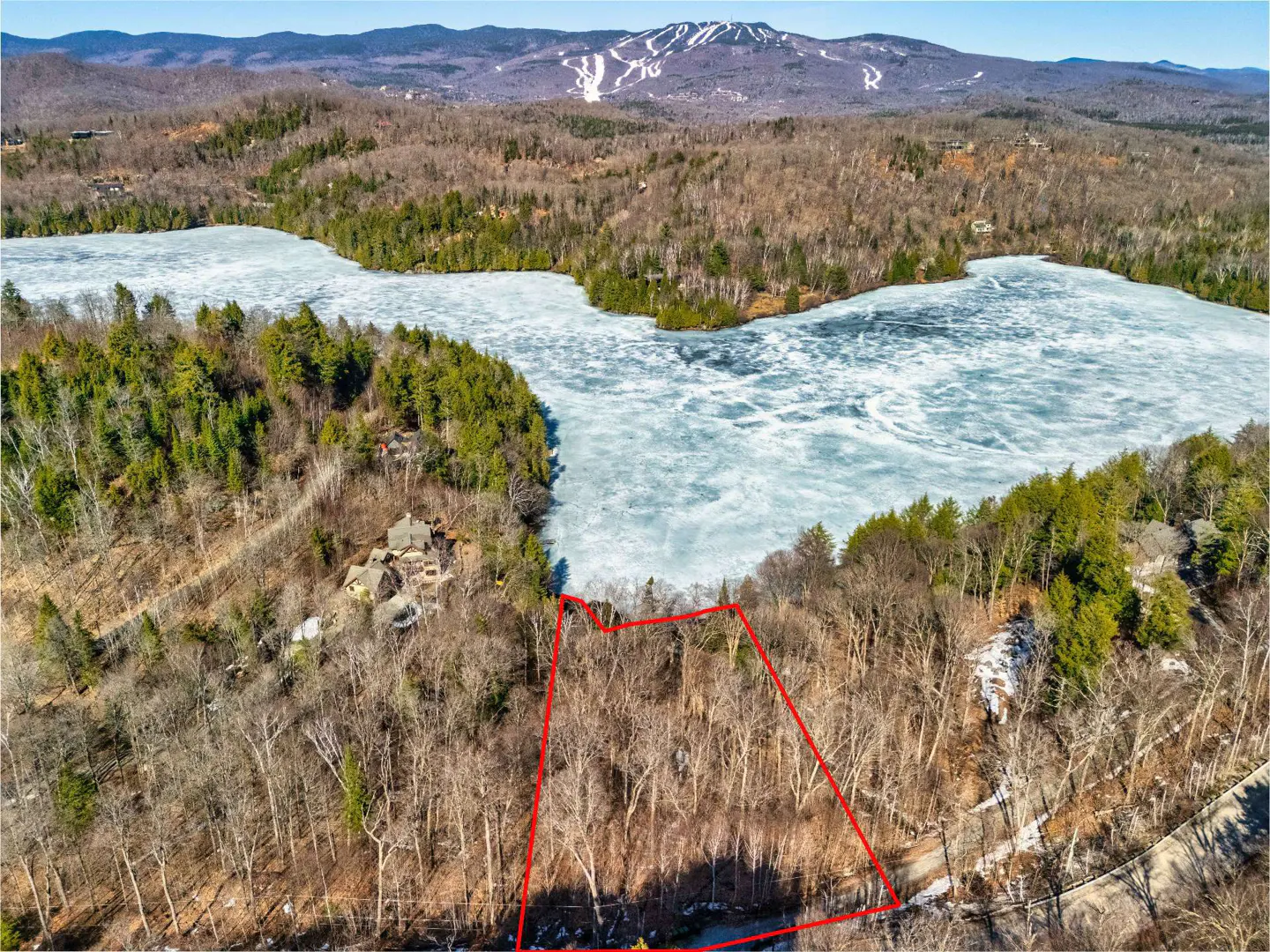 Aerial view of a wooded lot outlined in red, near a frozen lake and mountain with ski trails.
