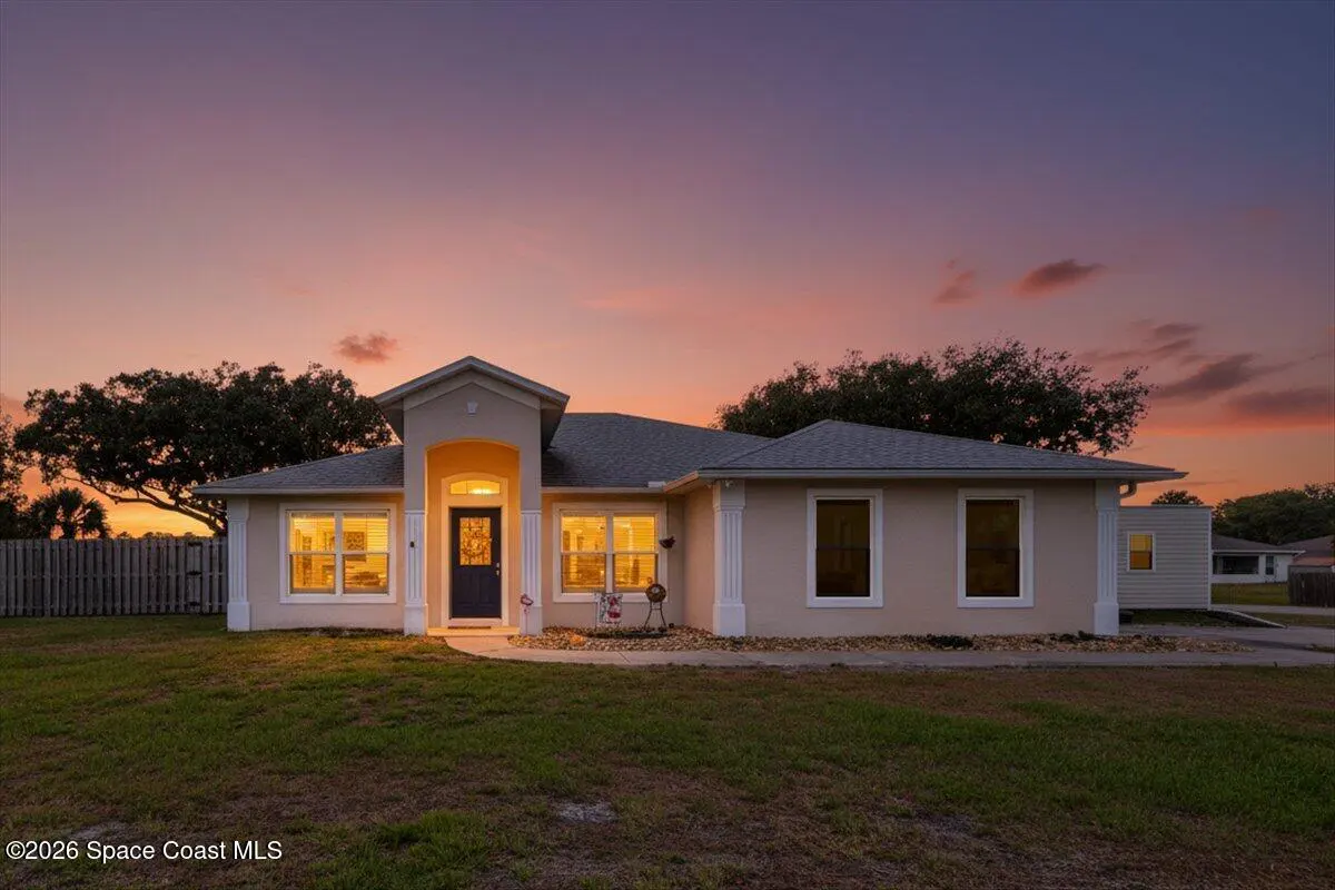Beige single-story home with a dark blue front door, set against a colorful sunset sky.