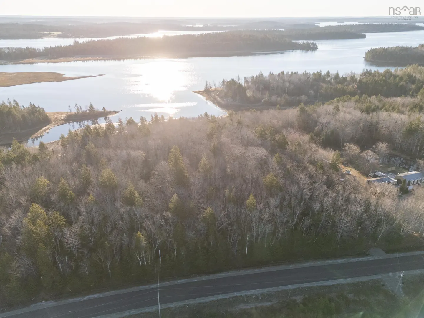 Aerial view of wooded land with a road in the foreground and a lake with islands in the background.