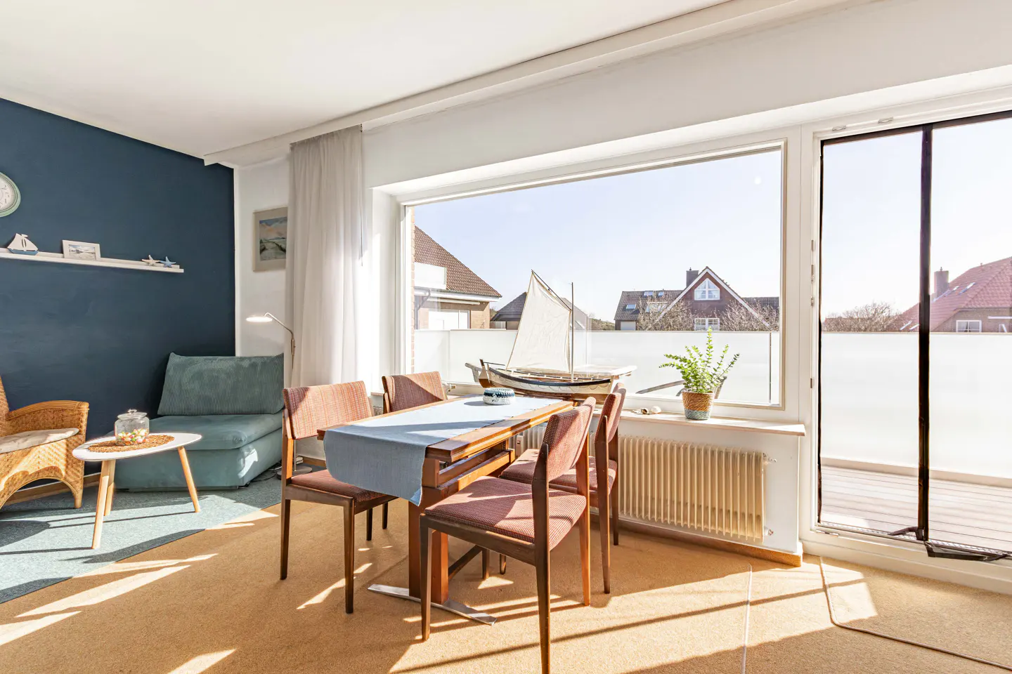 Bright living room with blue accent wall, dining table, and large window with a sailboat model.
