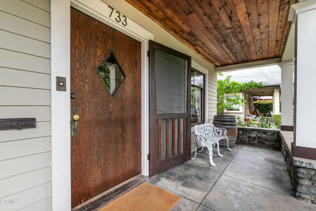 Front door of house number 733, with diamond window, open screen door, and white bench on porch.