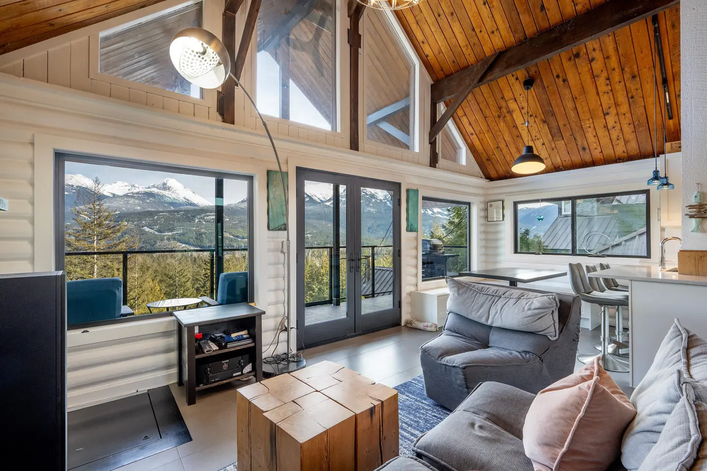 Living room with vaulted wood ceiling, large windows showing mountain views, gray sofa, and wood block coffee table.