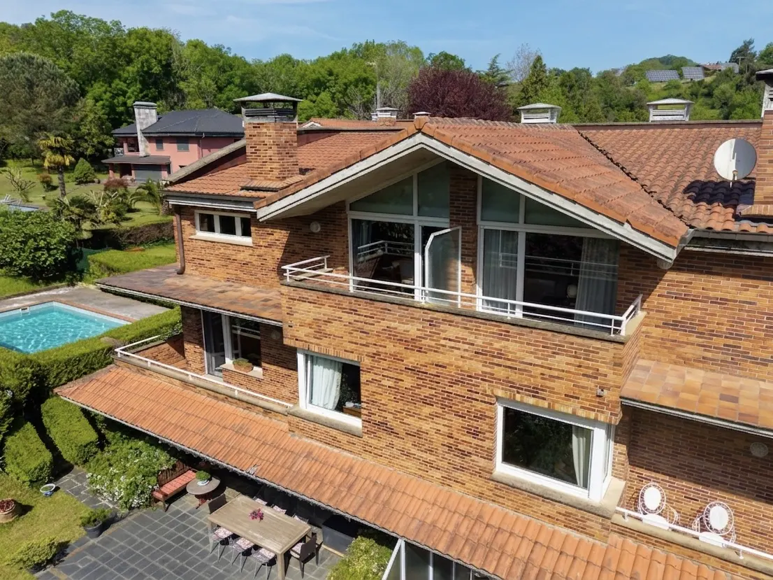 Aerial view of a two-story brick house with a red tile roof, a pool, and a patio with a table and chairs.
