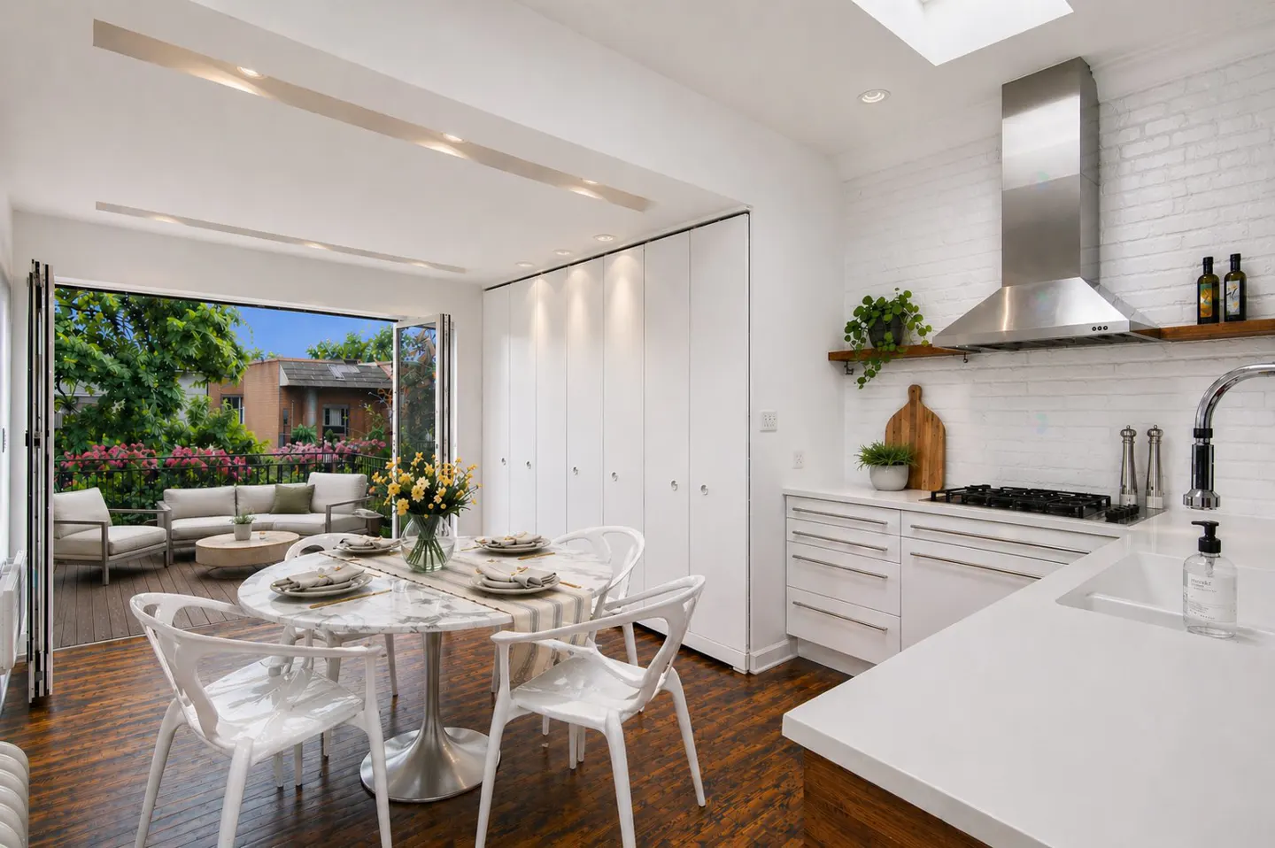 Bright, modern kitchen with white cabinets, stainless steel appliances, and a marble table set for dining. Open doors lead to a patio with outdoor seating.
