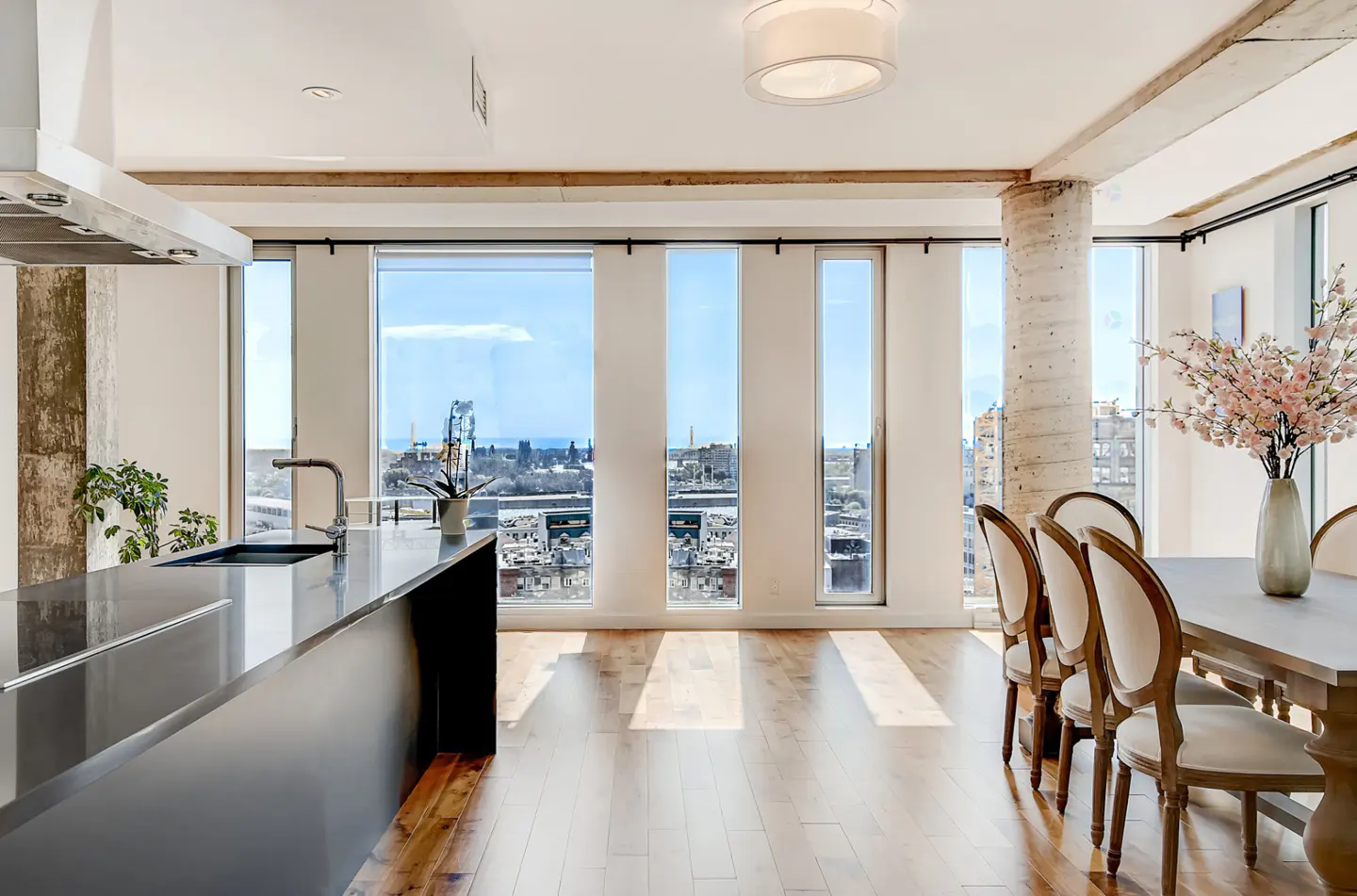 Bright, open-concept kitchen and dining area with hardwood floors and city views from large windows. Black island, dining table with chairs, and floral arrangement.
