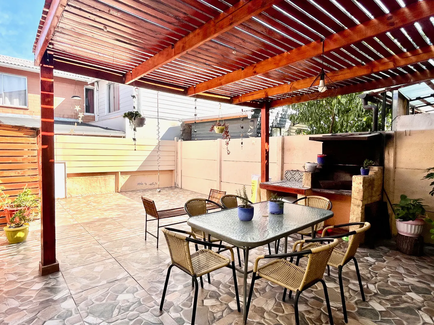 Outdoor patio with a wooden pergola, stone tile floor, table with chairs, and a built-in stone barbecue.