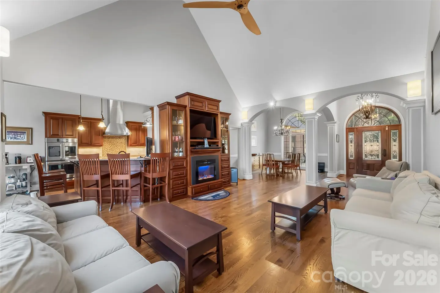 Open-concept living space with hardwood floors, white sofas, and a kitchen with wood cabinets and bar seating. A wooden entertainment center is visible.