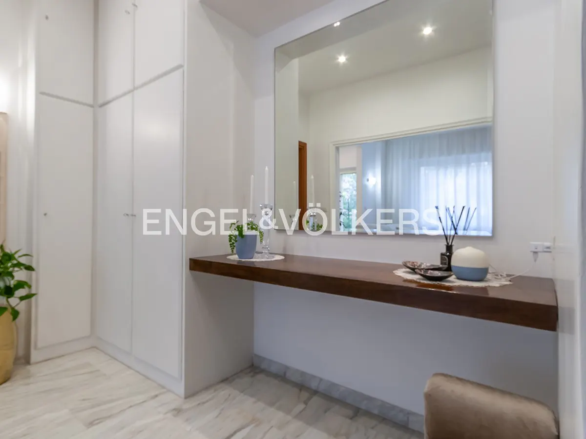 Interior view of a white room with a wood shelf, mirror, and white cabinets. Candles and decor sit on the shelf. Marble flooring.