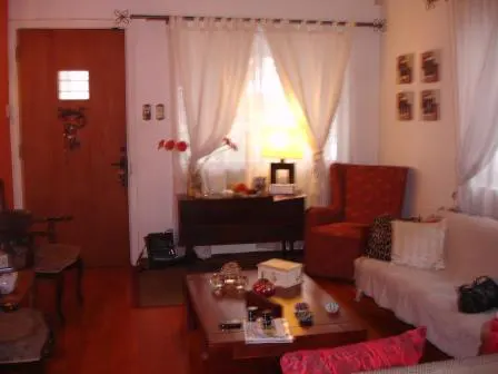 A cozy living room with a wooden door, red armchair, white sofa, and a dark wood coffee table. White curtains filter light from the window.