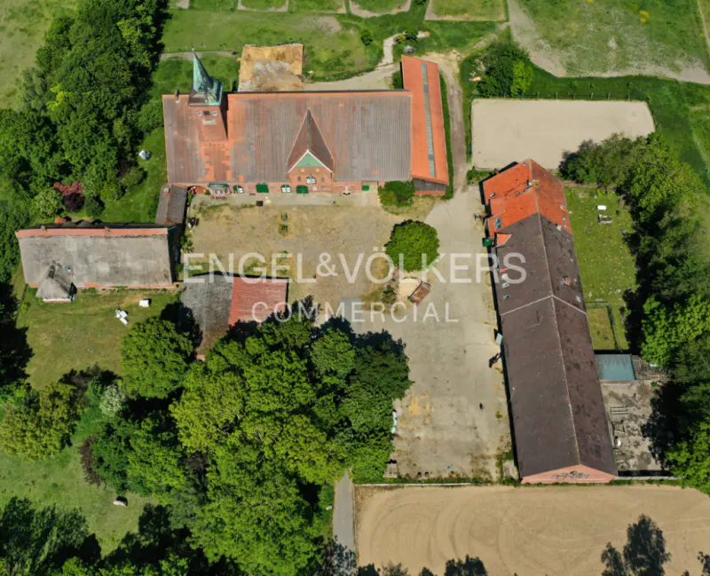 Aerial view of a commercial property with red-roofed buildings, green trees, and a large courtyard. The Engel & Völkers logo is visible in the center.