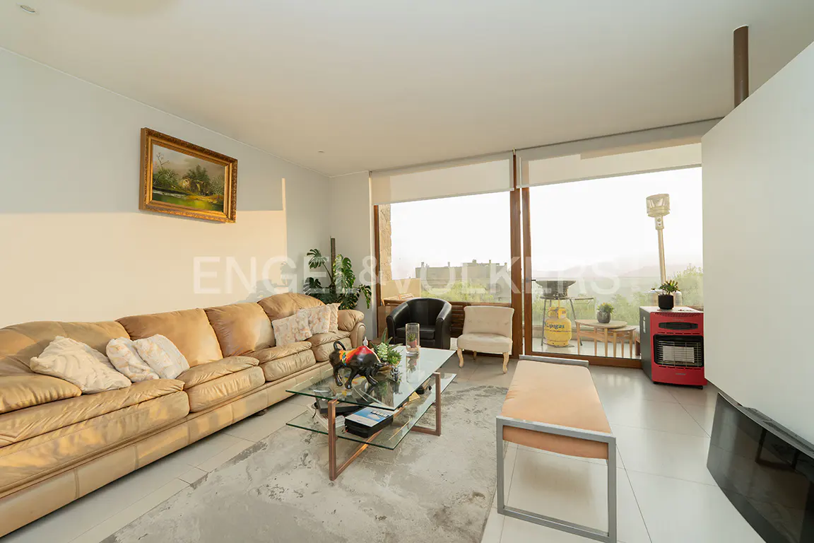 Living room with a tan leather sofa, glass coffee table, and floor-to-ceiling windows. A painting hangs on the wall.