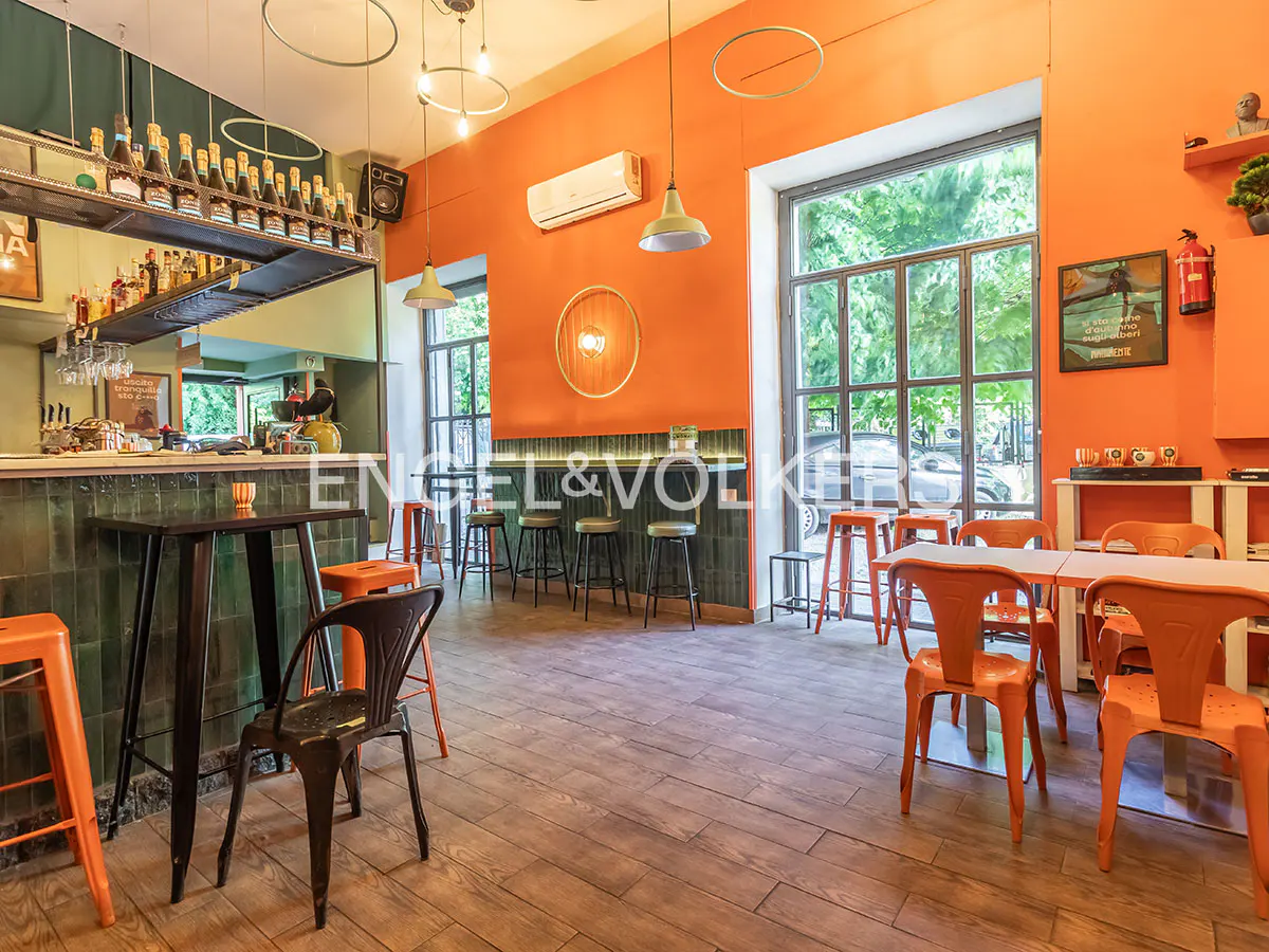 Interior view of a bar with orange walls, wooden floors, tables, chairs, and a bar with bottles on shelves.