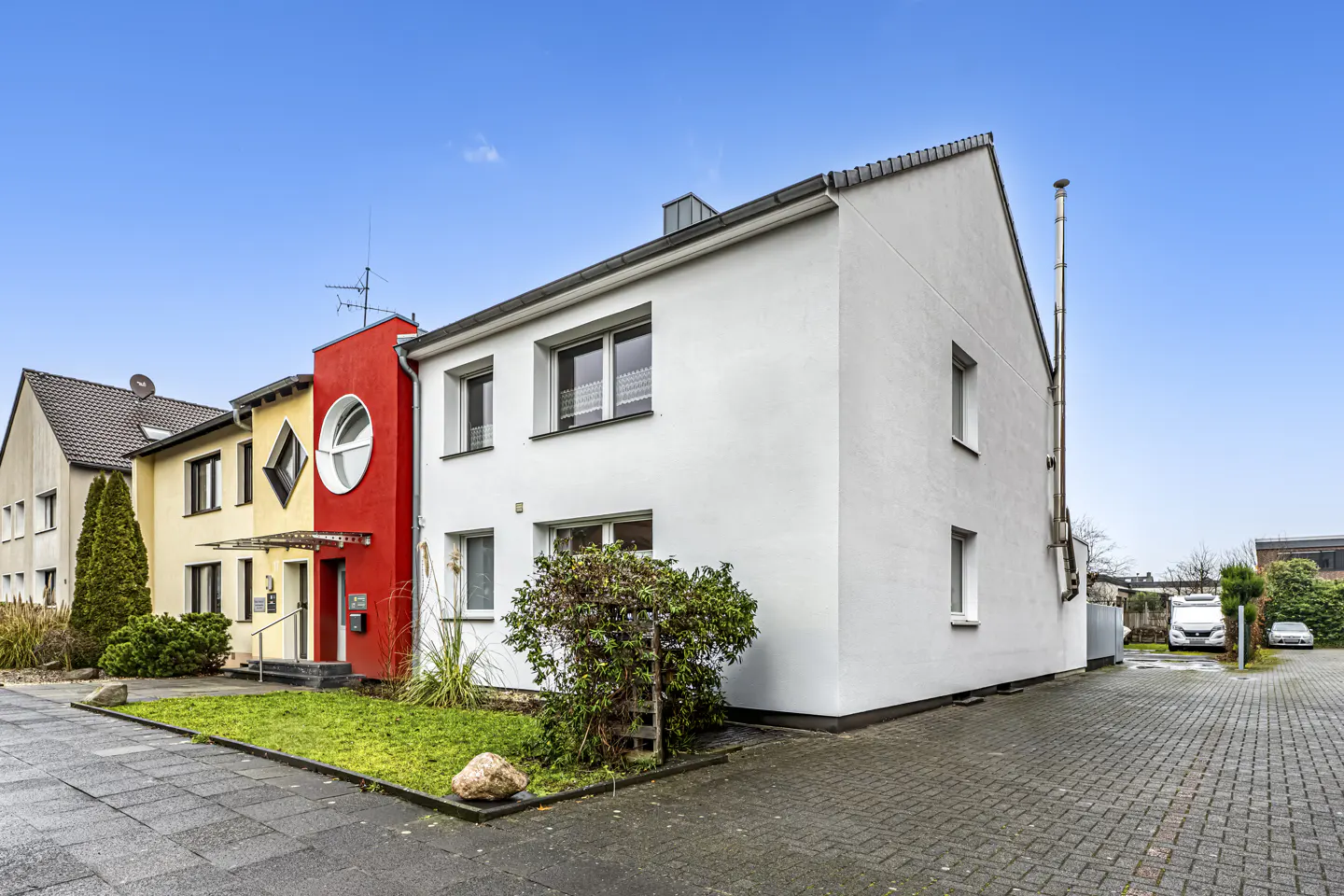 Exterior view of a modern, two-story townhouse with white facade, red accent wall, and a round window. Blue sky background.