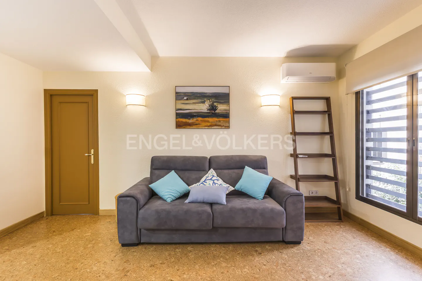 Living room with gray sofa, blue pillows, wood ladder shelf, and cork floor. Painting on the wall.