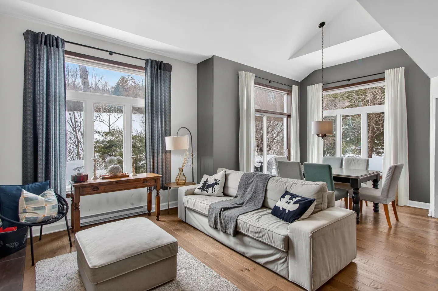 Living room with hardwood floors, a beige sofa, and large windows overlooking a snowy landscape.