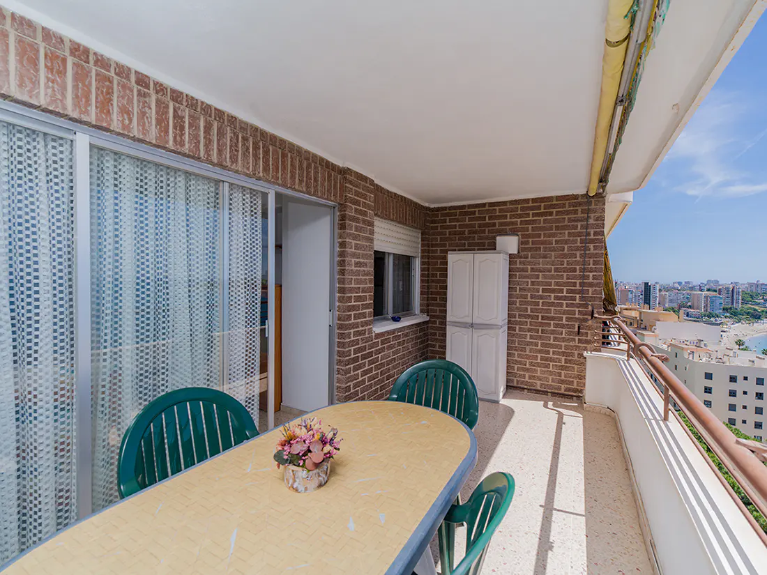 Balcony view with table, chairs, and city skyline. Brick walls and a sliding glass door are visible.