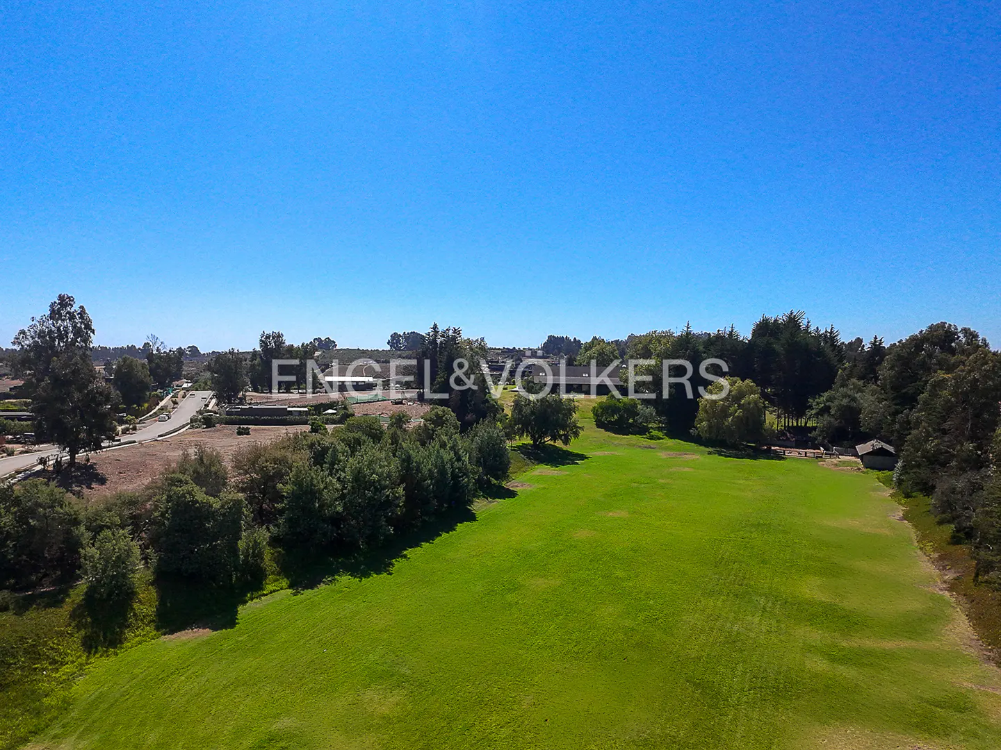 Aerial view of a lush green lawn with trees, a building, and a clear blue sky.