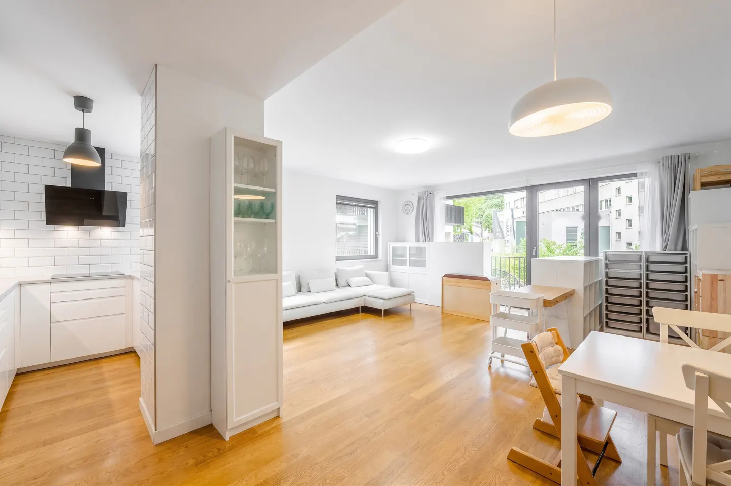 Bright open-plan apartment with a white kitchen, wooden floors, a living area with a sofa, and a dining space.