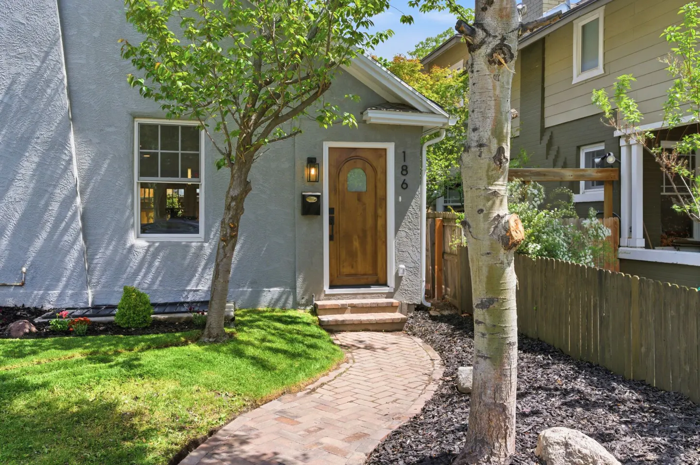 Front view of a gray stucco house with a wood door, brick path, and green lawn.