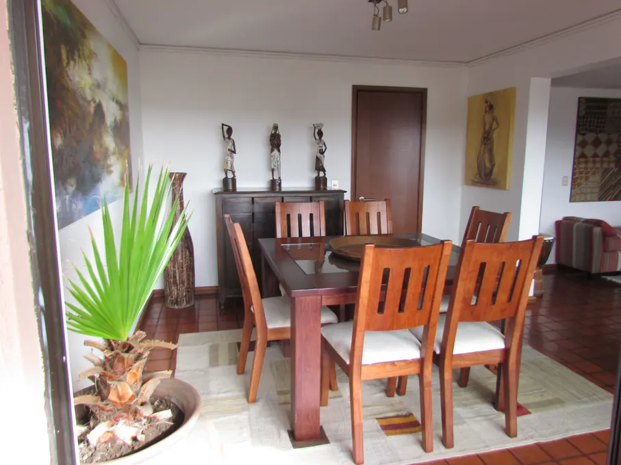 A dining room with a dark wood table and chairs, a dark wood cabinet with African statues, and artwork on the walls.