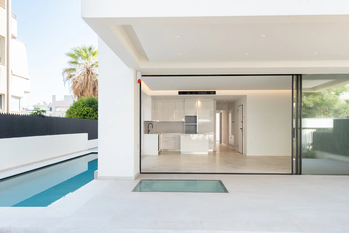 A modern, white kitchen is viewed from a patio with a pool through sliding glass doors.