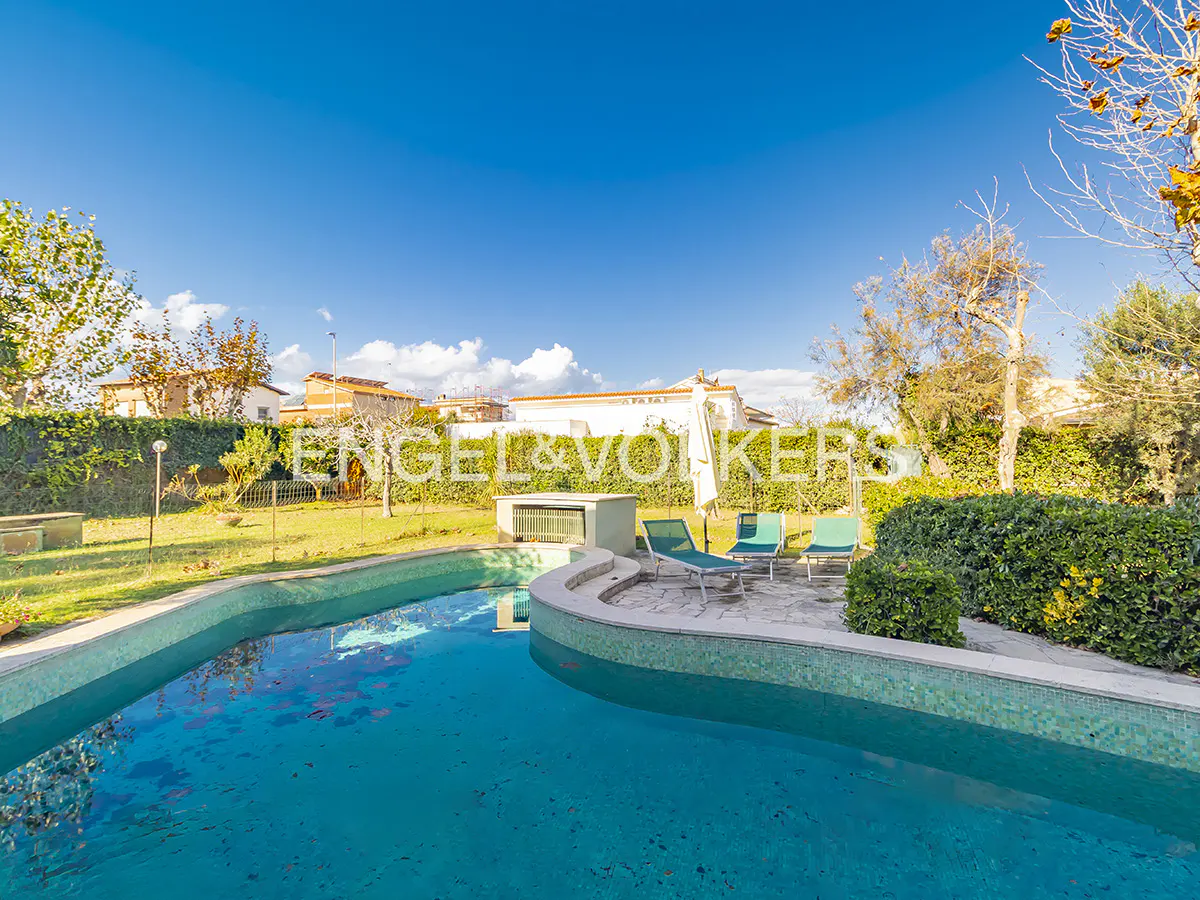 A backyard with a pool, lounge chairs, green grass, and the Engel & Volkers logo.