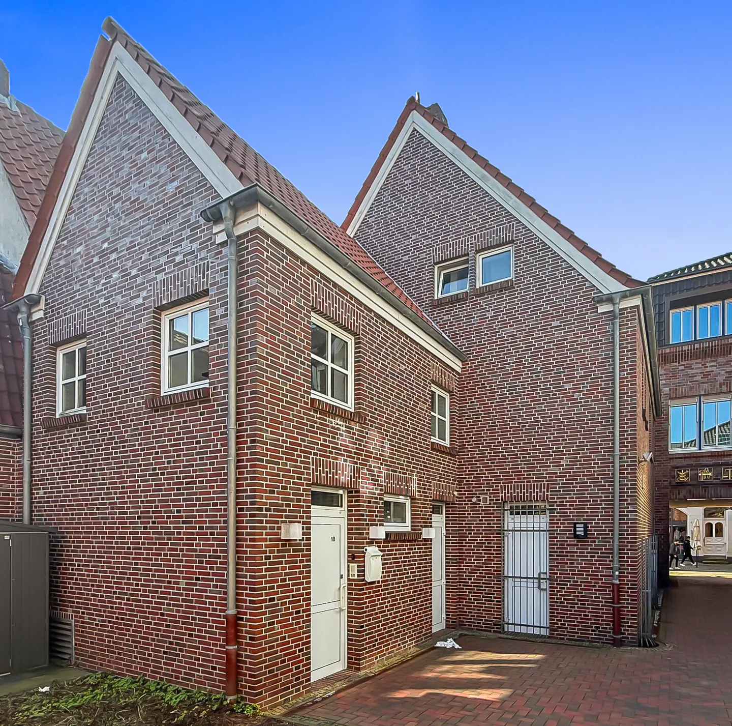 Exterior view of a two-story brick building with a red tile roof and white trim under a blue sky.
