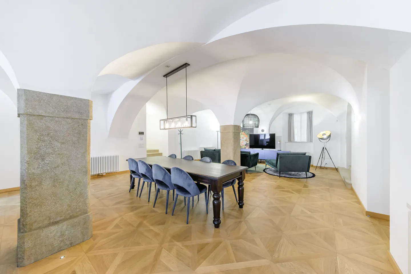 Bright, open-concept living space with vaulted ceilings, wood floors, dining table with blue chairs, and a living room area.