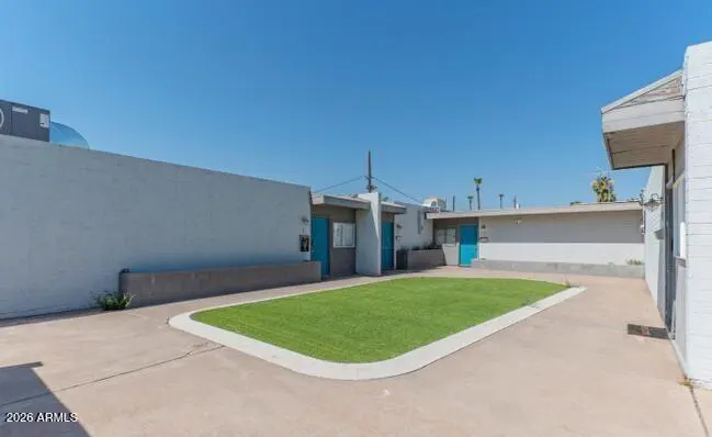 Exterior view of a building with a rectangular patch of green grass in the center, surrounded by concrete. Blue doors are visible on the building.
