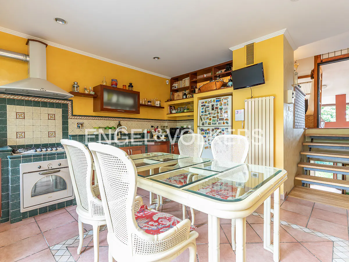 Dining area with a glass-top table, white wicker chairs, yellow walls, tiled floors, and a kitchen with a white oven.