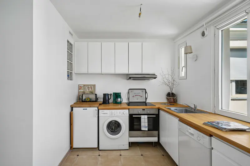 Bright, compact kitchen with white cabinets, wood countertops, and appliances including a washing machine. A window provides natural light.