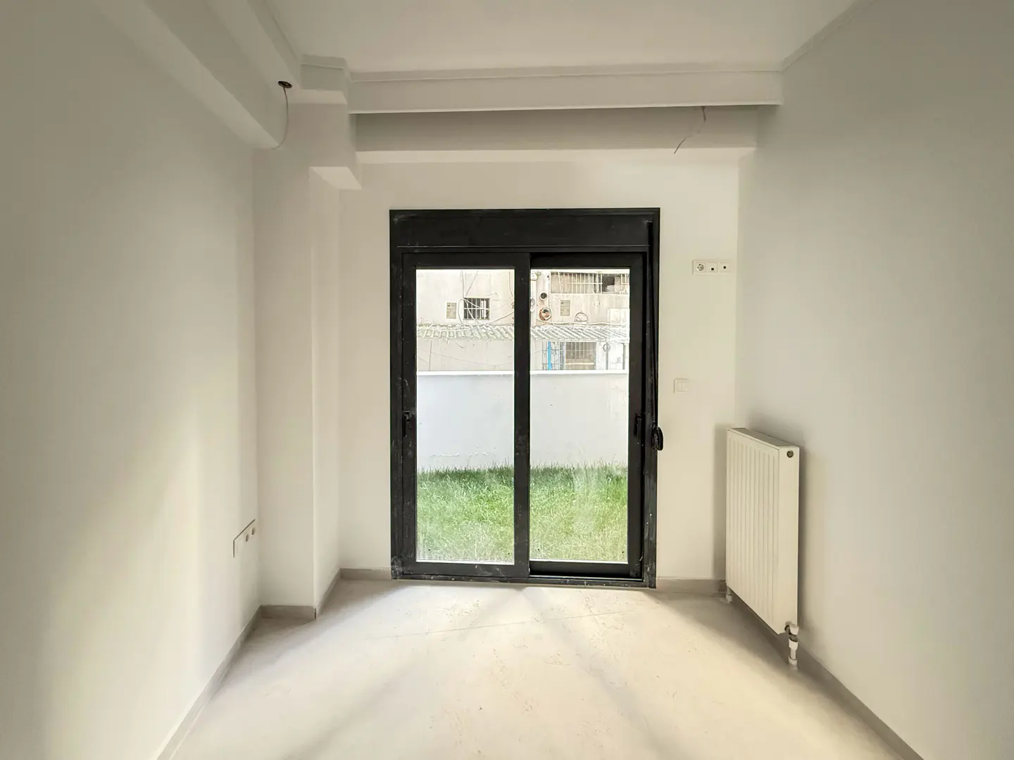 Empty room with white walls, a radiator, and a black sliding glass door to a grassy yard.