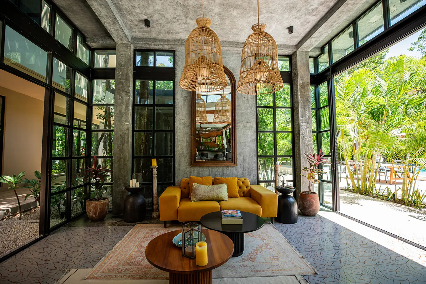 Bright living room with concrete walls, black framed windows, and a yellow sofa. Two rattan pendant lights hang above a wooden coffee table.