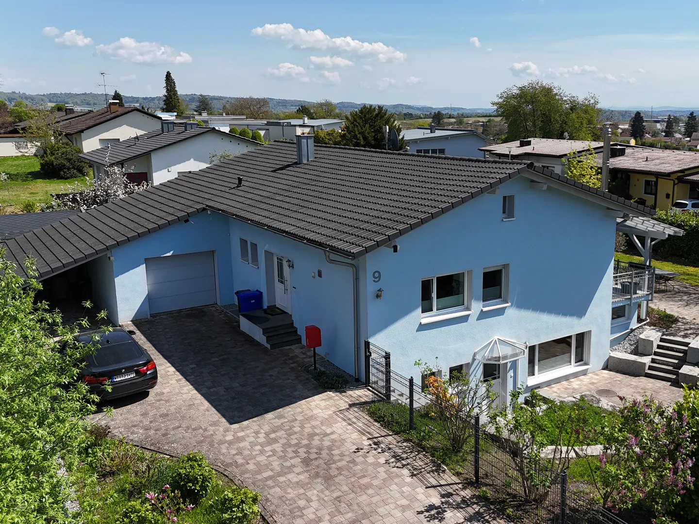 A light blue, single-family home with a dark gray roof, a driveway, and a car parked in the carport.