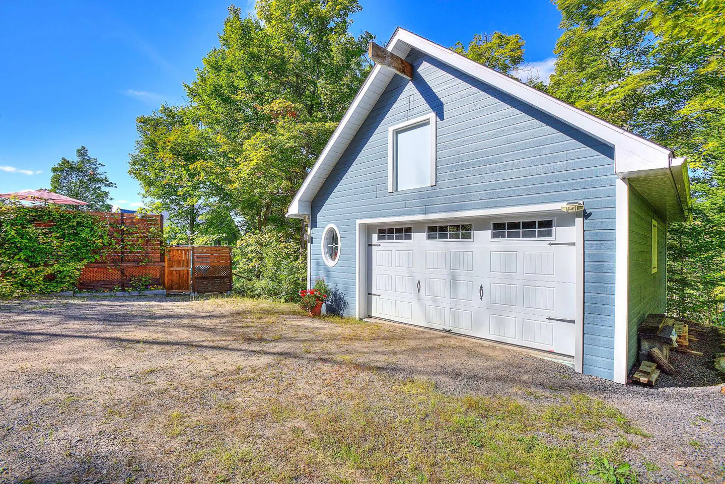 A light blue garage with a white door and trim, set against a backdrop of green trees and a blue sky.