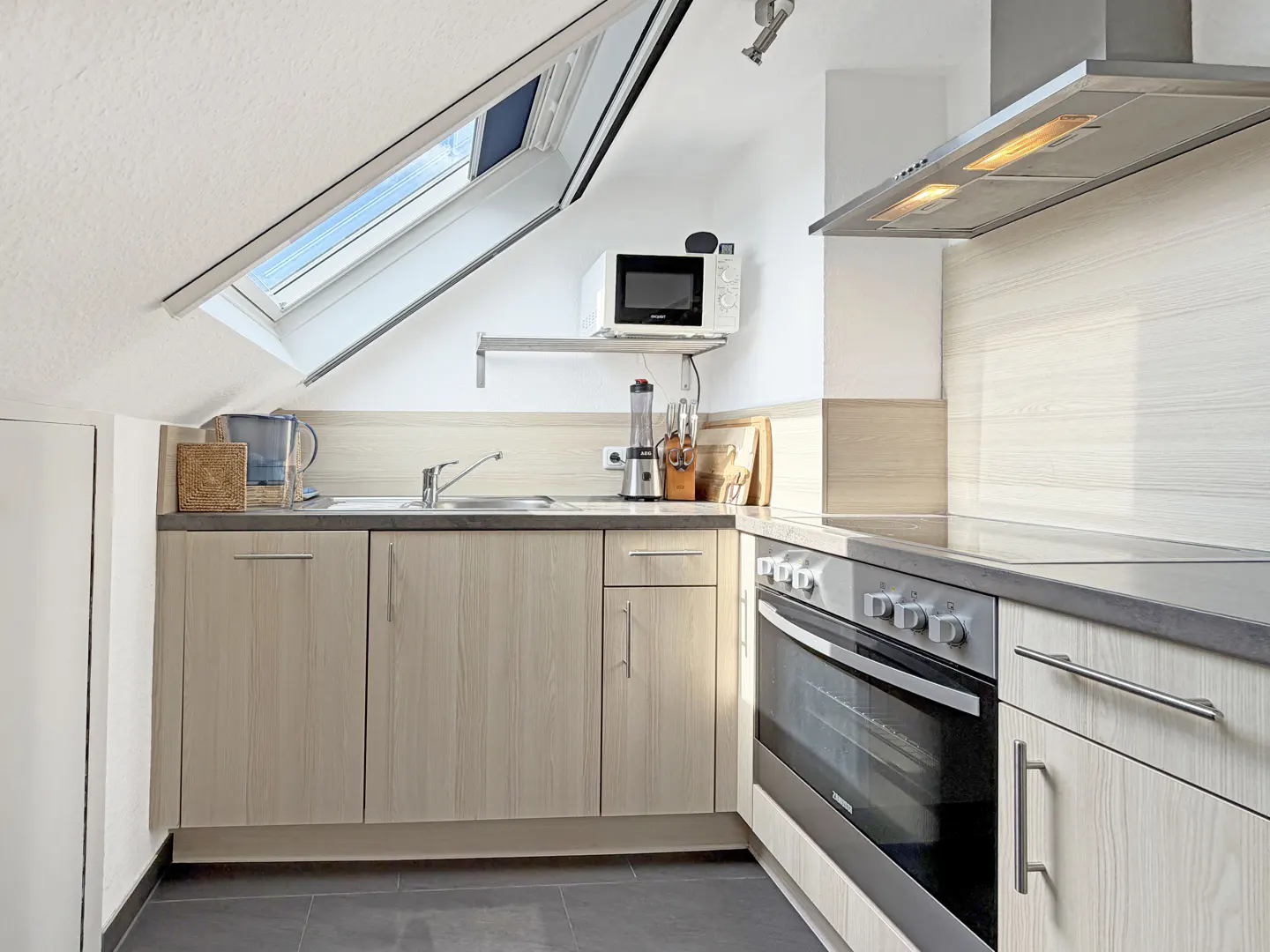 Bright kitchen with light wood cabinets, gray countertops, and stainless steel appliances. A skylight illuminates the space.