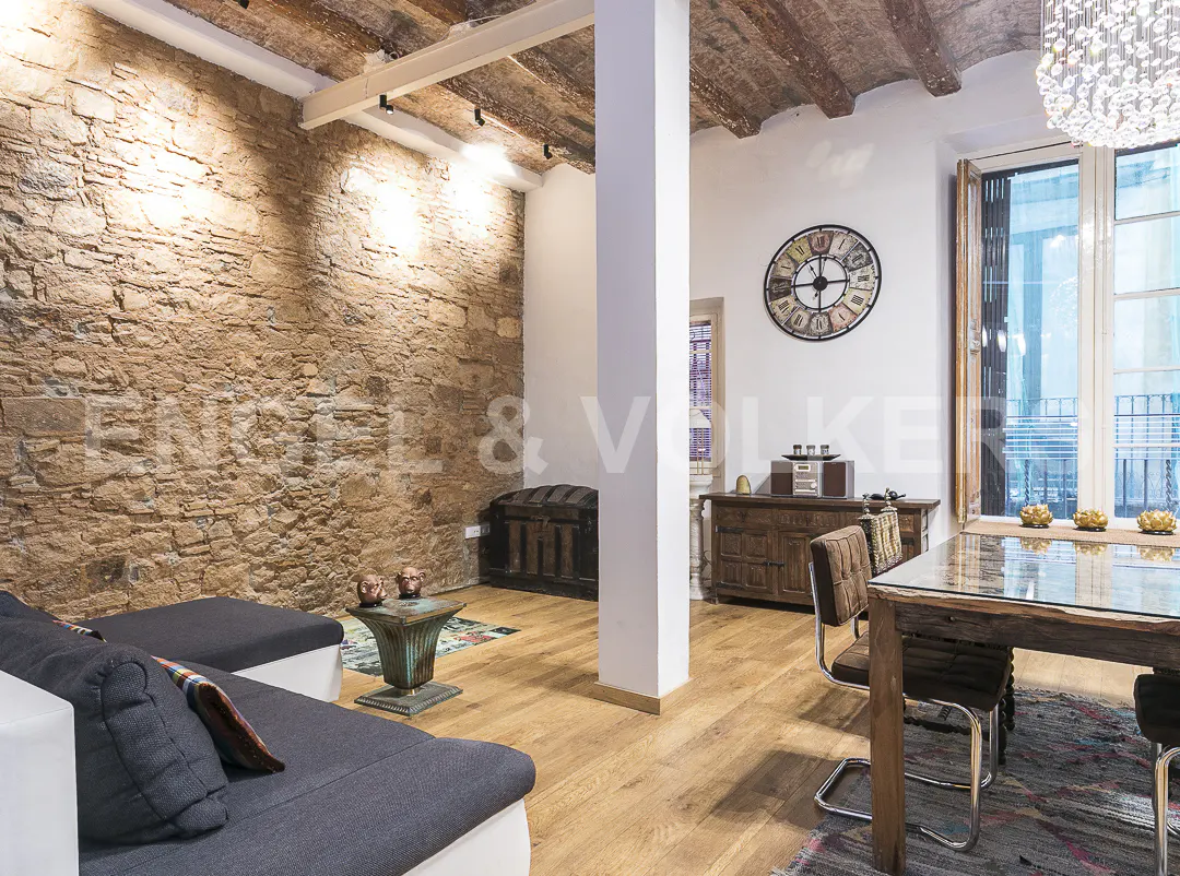Living room with stone wall, gray sofa, wooden table and chairs, and a large clock on the wall.