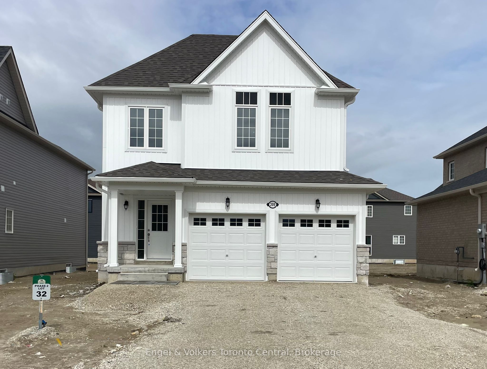 Two-story white house with a gray roof and a two-car garage. The house has white trim and black windows. A sign in the yard reads "Phase 2 Lot 32".