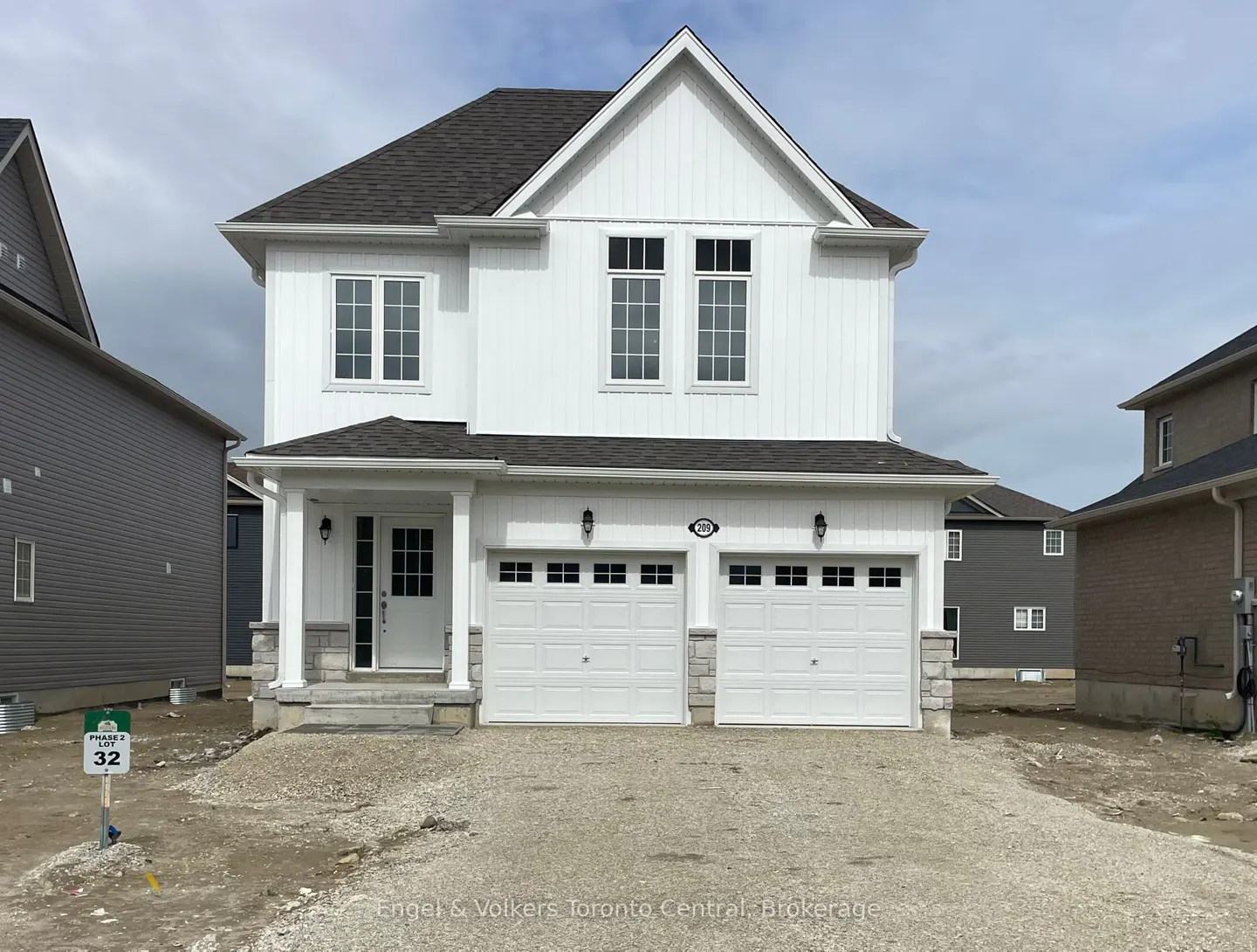 Two-story white house with a gray roof and a two-car garage. The house has white trim and black windows. A sign in the yard reads "Phase 2 Lot 32".