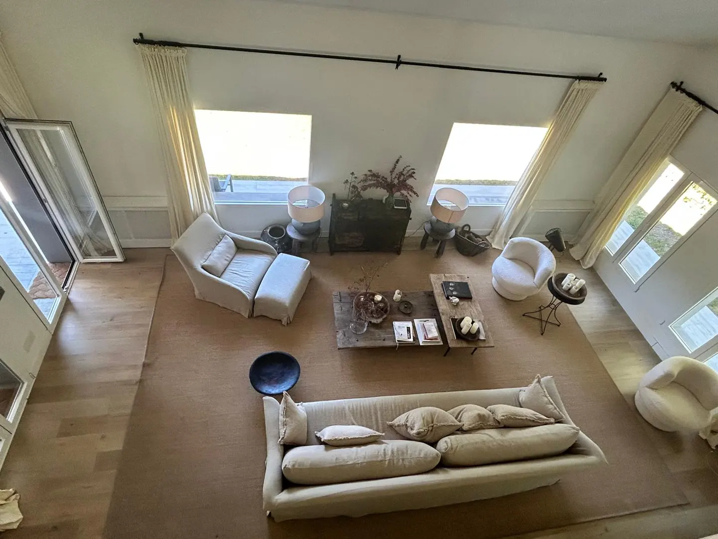 High-angle view of a bright, modern living room with a beige sofa, armchairs, and wooden coffee tables on a large rug.