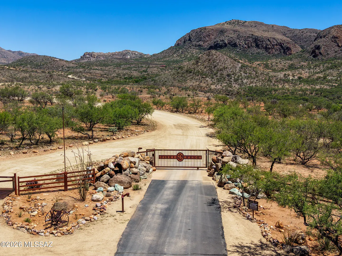 Gated entrance to Sabino Ranch with desert landscape and mountains in the background under a clear blue sky.