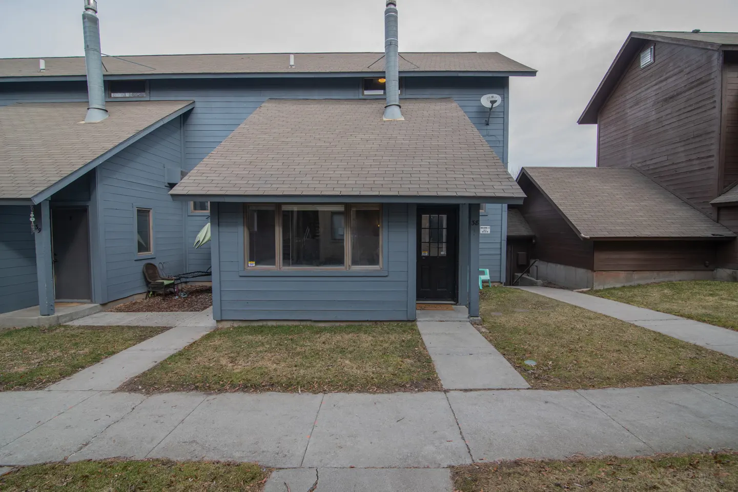 Exterior of a blue townhouse with a brown roof and a black front door. A concrete walkway leads to the entrance.