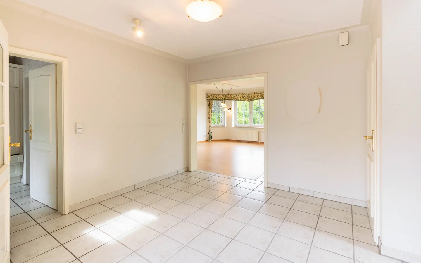 Bright, empty room with white tile floor, cream walls, and open doorways to other rooms.