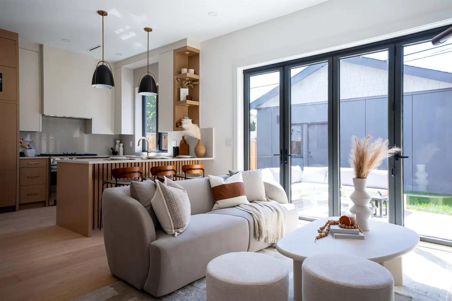 Open-concept living space with a gray sofa, white coffee table, and kitchen island. Black-framed glass doors lead to a patio.